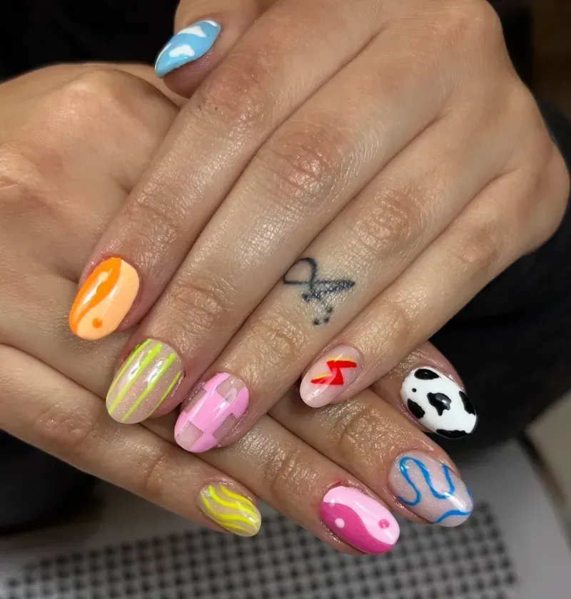 Arte de uñas colorido con diseños que incluyen nubes, estampados de vaca y rayos en las manos de una persona.
