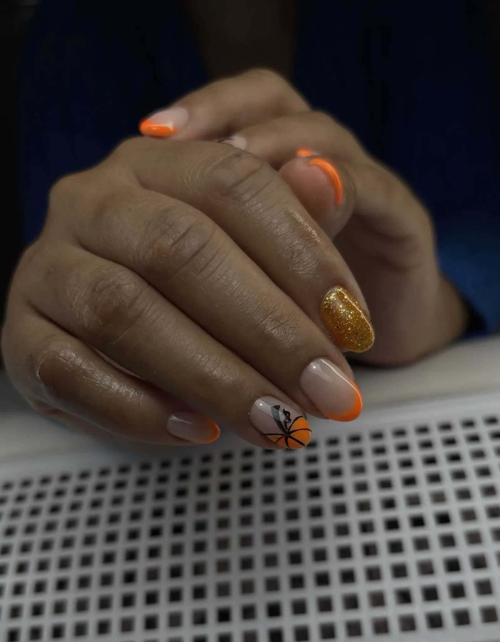 Manos con arte de uñas con temática de Halloween en tonos naranja y dorado, incluido un diseño de araña.