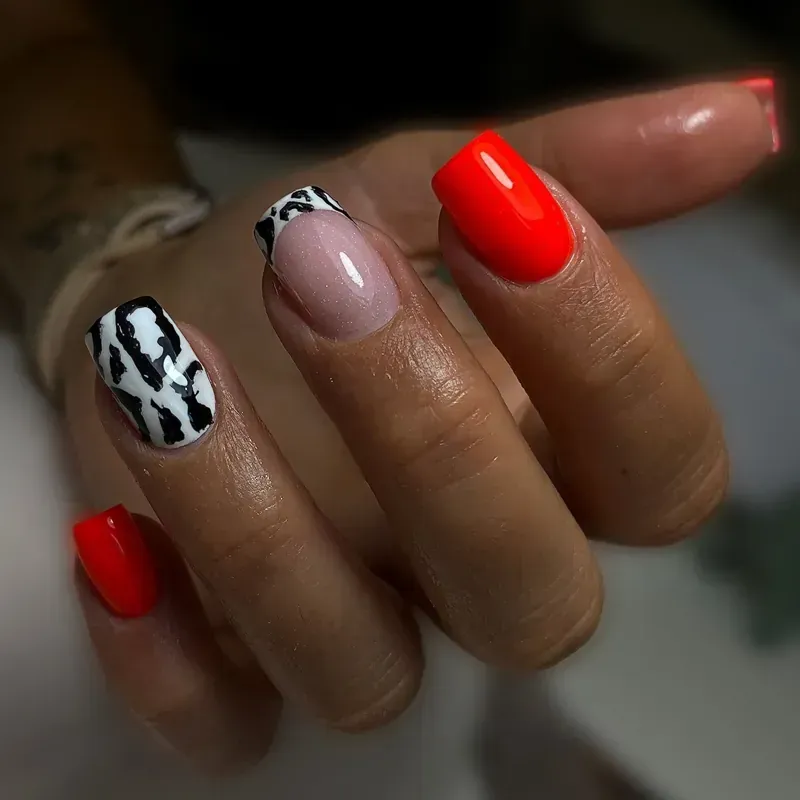Primer plano de una mano con uñas rojas y con estampado animal. Una uña tiene un diseño de punta francesa.