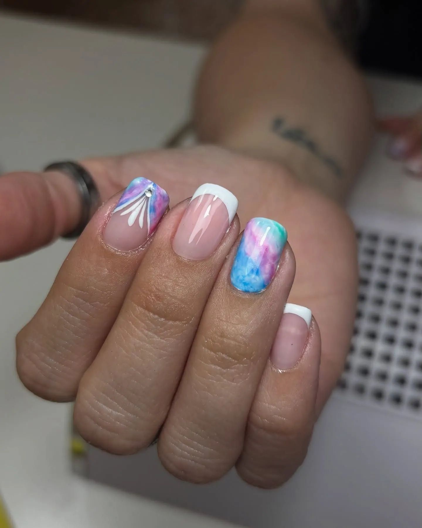 Mano con uñas cuidadas: puntas francesas, diseño abstracto de acuarela y diseño de hojas blancas.
