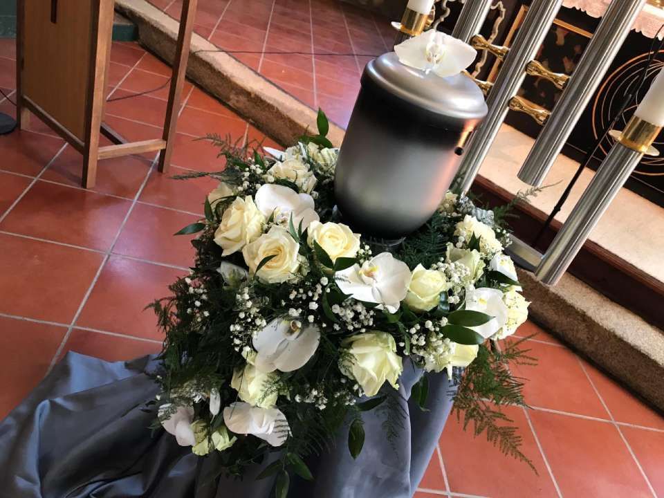 Graue Urne auf Blumenschmuck mit weißen Rosen