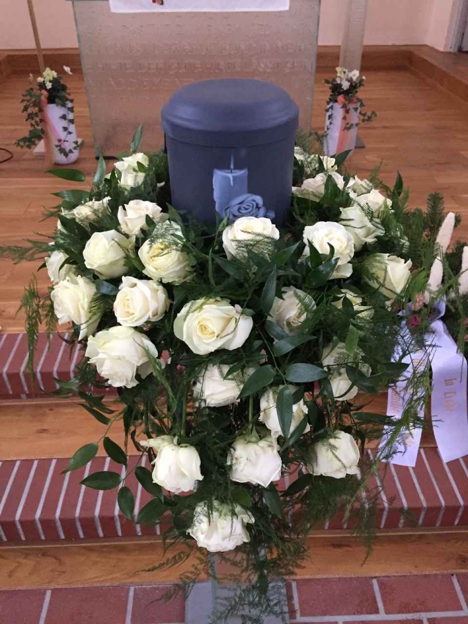 Lilafarbene Urne auf weißem Rosenschmuck