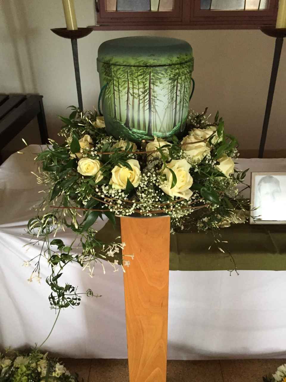 Grüne Urne mit Baummotiv auf einem Blumenarrangement