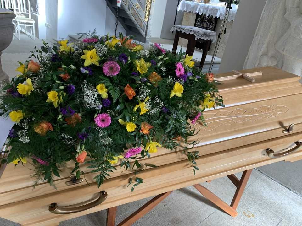 heller Holzsarg mit Blumenarrangement