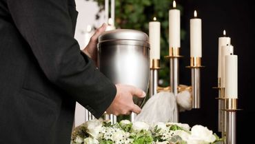 Person hält Urne vor Kerzen und Blumenarrangement