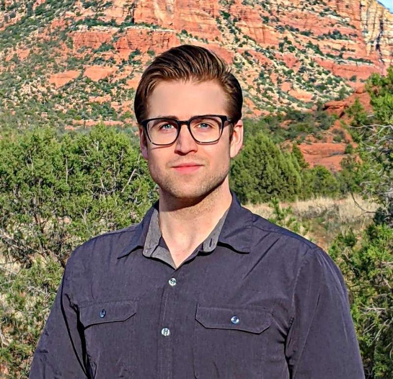 Man wearing glasses and button-down shirt outdoors with red rock mountain in the background.
