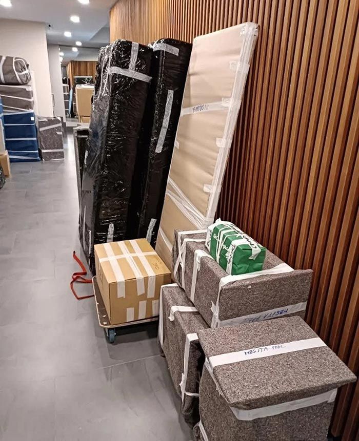 Muebles apilados y cajas envueltas en un pasillo, con paneles de listones de madera en la pared cerca.