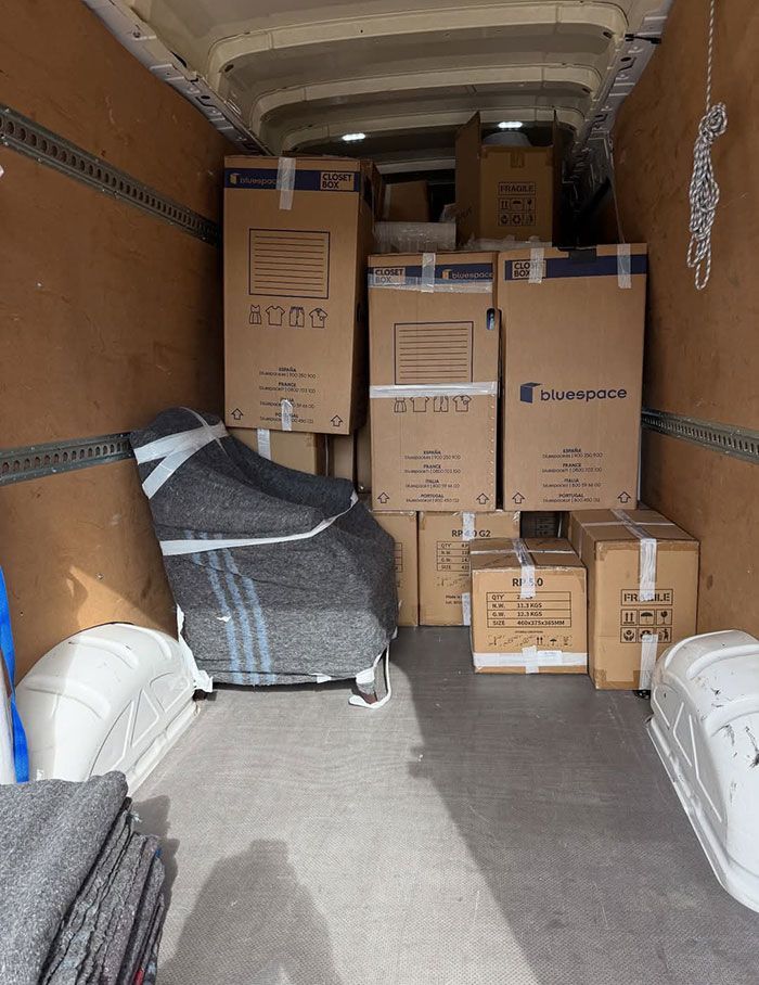 Interior de camión de mudanzas repleto de cajas de cartón apiladas y muebles envueltos.