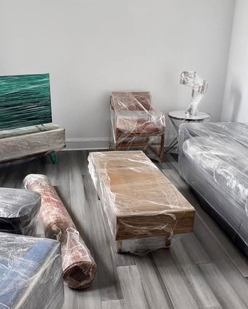 Muebles embalados y artículos domésticos envueltos en una habitación con suelo gris.