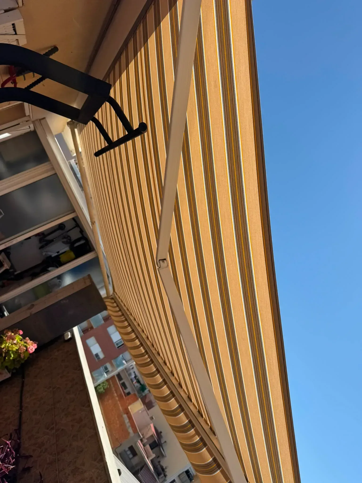 Toldo amarillo a rayas en el exterior de un edificio contra un cielo azul, visto desde un ángulo