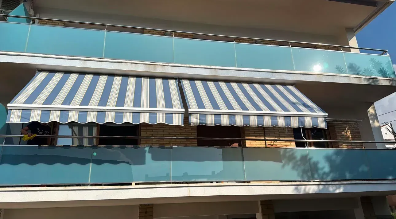 Fachada azul del edificio con un gran toldo a rayas azules y blancas sobre las ventanas.