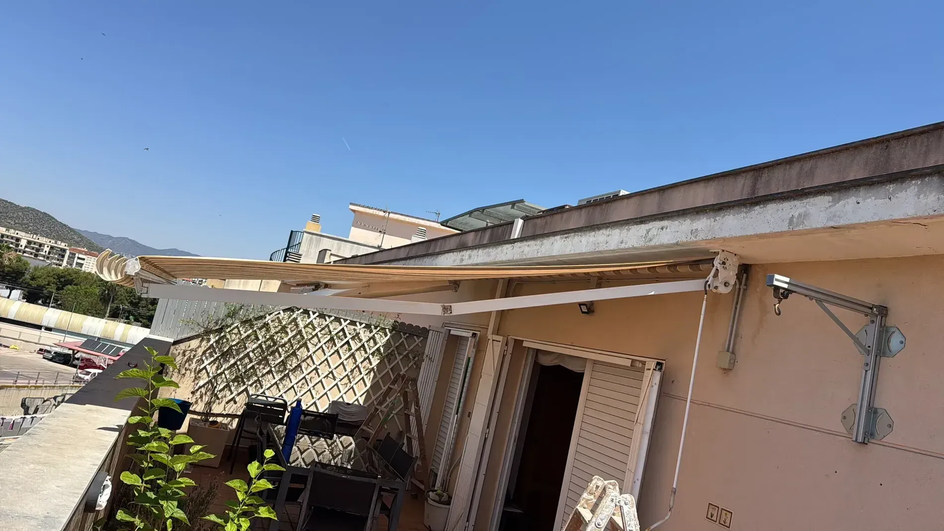 Exterior de una casa bañada por el sol, con toldo beige, pilares blancos