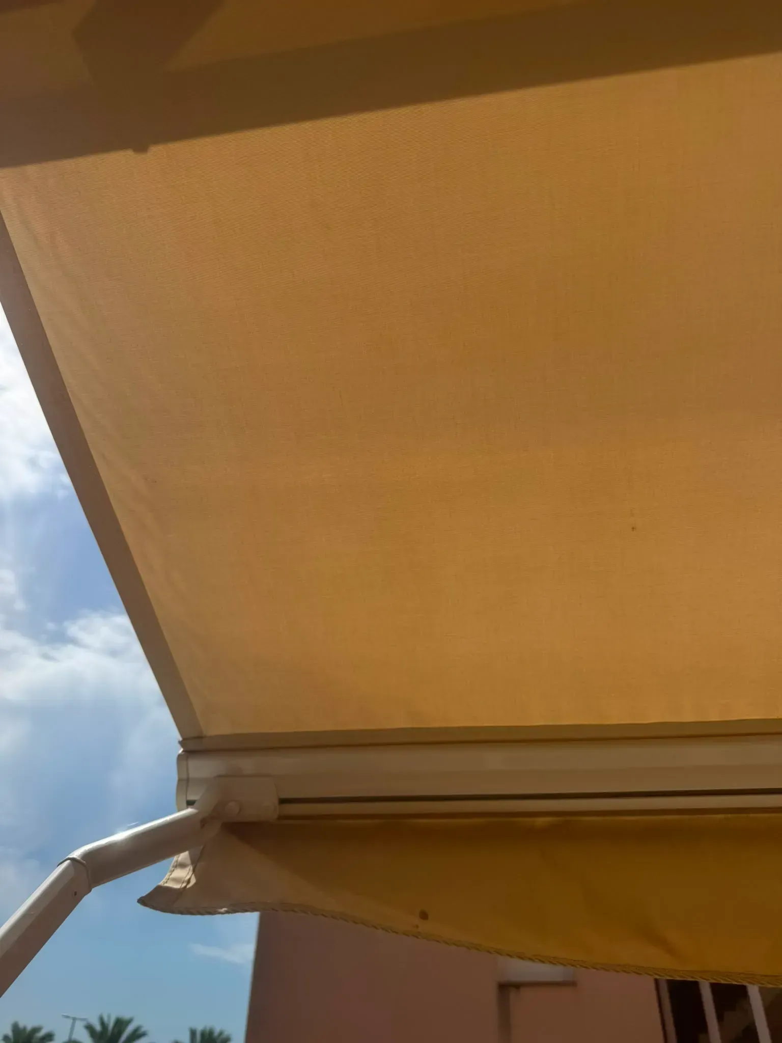 Toldo beige visto desde abajo contra un cielo azul con nubes.
