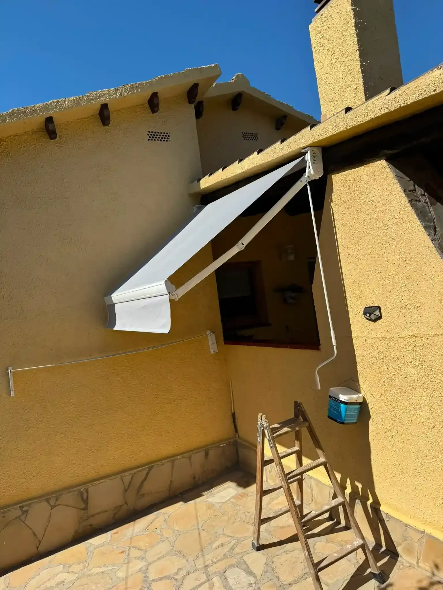 Patio con un toldo retráctil blanco que se extiende sobre una pared de estuco color canela y una escalera debajo.