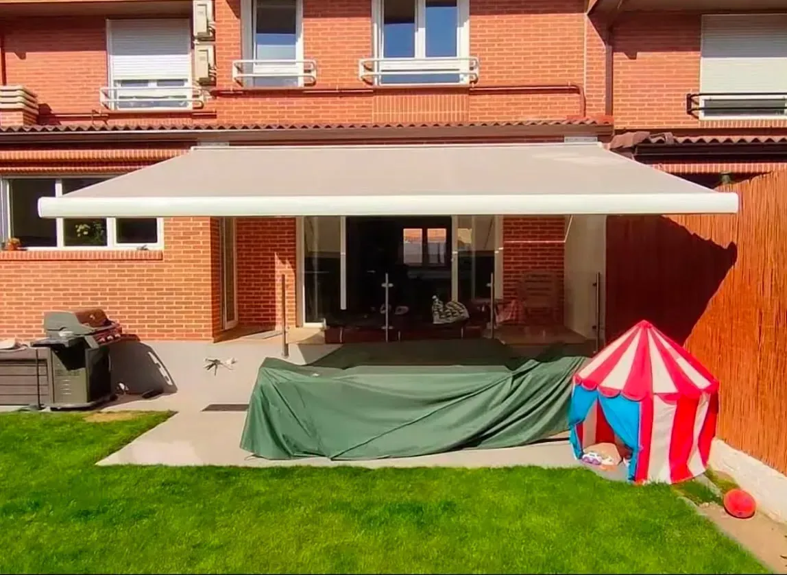 Patio trasero con toldo blanco, mesa cubierta con una manta verde y una pequeña tienda de juegos a rayas rojas y blancas.