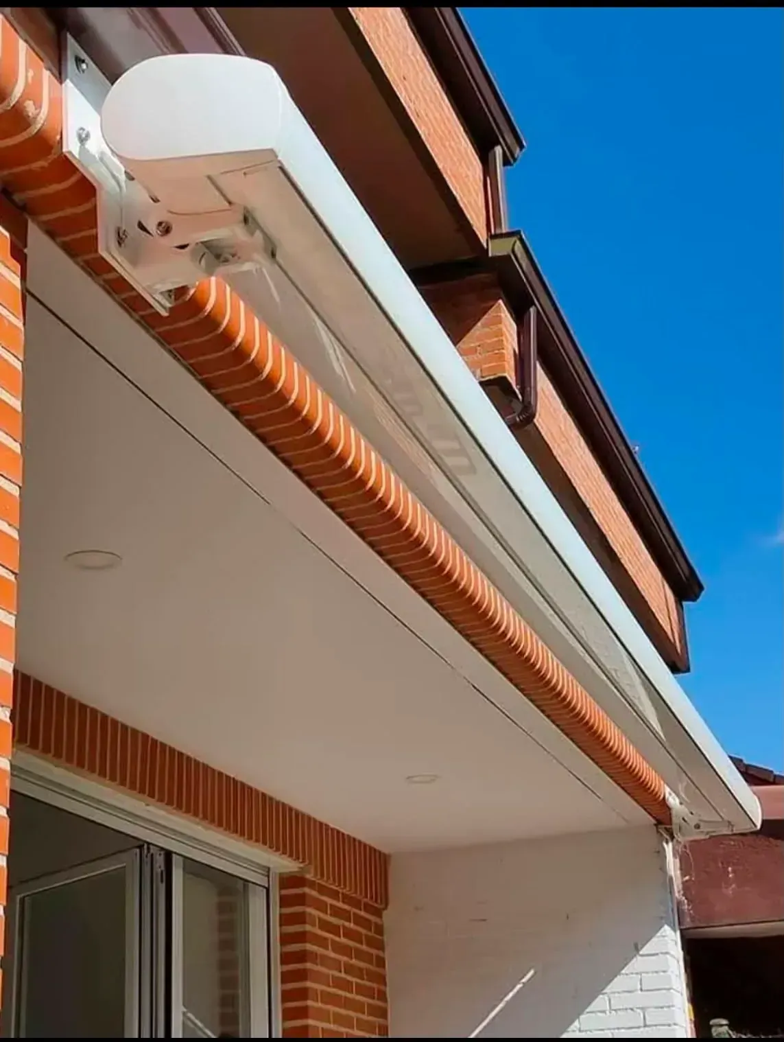 Toldo retráctil blanco en la fachada de una casa de ladrillo contra un cielo azul.