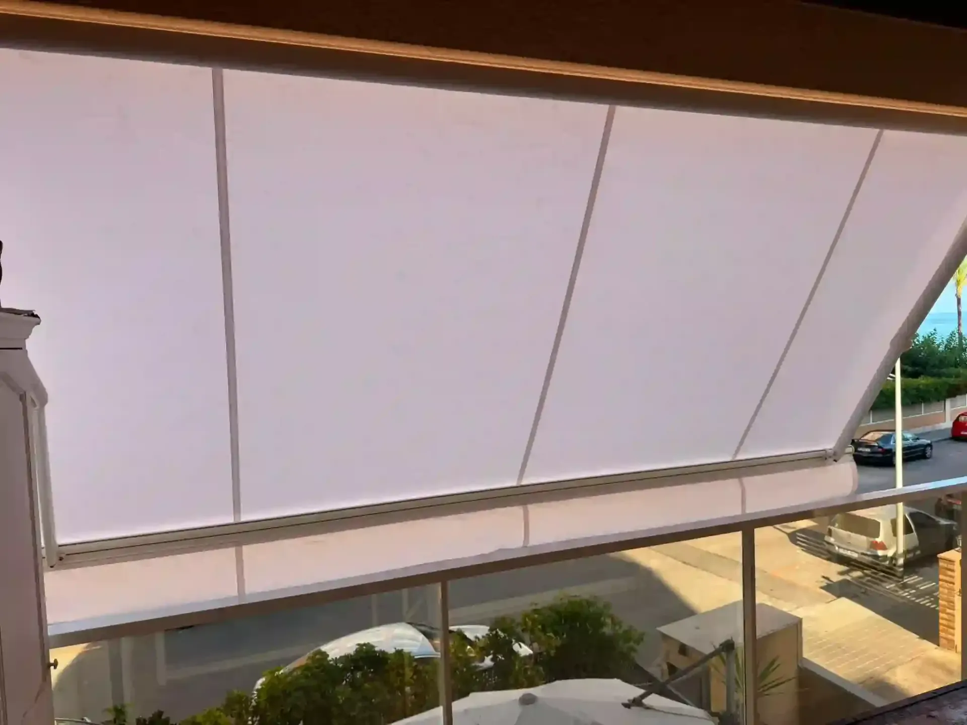 Un gran toldo blanco se extiende sobre un patio junto a un edificio, con asientos al aire libre debajo.