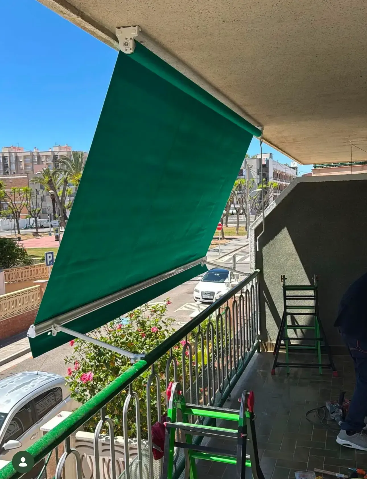 Un toldo verde se extendía sobre un patio con barandilla, sillas y vistas a la ciudad.