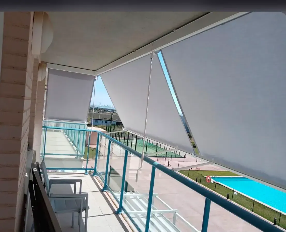Balcón con barandillas color turquesa, toldos blancos y vistas a la piscina bajo la luz del sol.