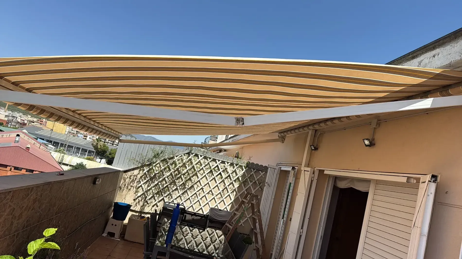 Patio trasero con toldos a rayas, pérgola y exterior de la casa bajo un cielo azul despejado.