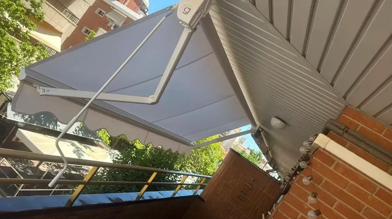 Toldo triangular blanco sobre un patio de ladrillos, visto en ángulo junto a una casa.
