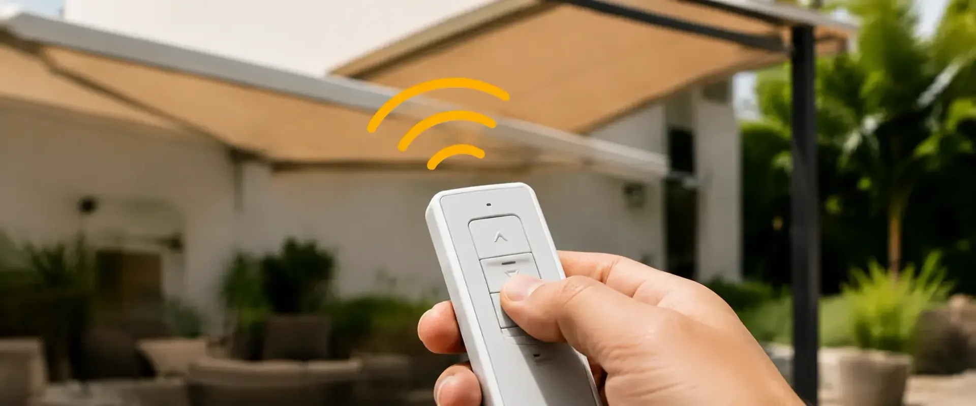 Una mano sostiene un control remoto blanco y apunta hacia el toldo de un patio exterior.