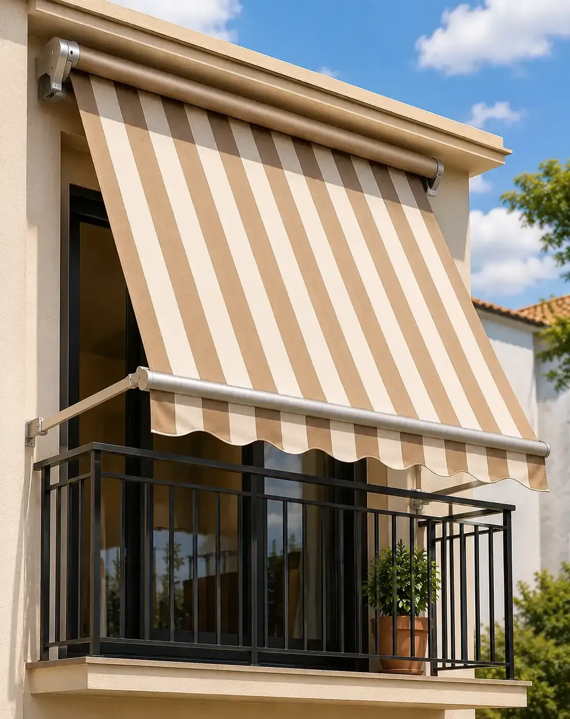 Toldo a rayas beige y blancas sobre un pequeño balcón con barandilla negra y una planta en maceta.