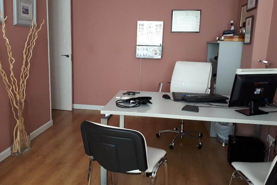 Oficina vacía con escritorio, ordenador, silla blanca y suelo de madera marrón sobre paredes rosas.