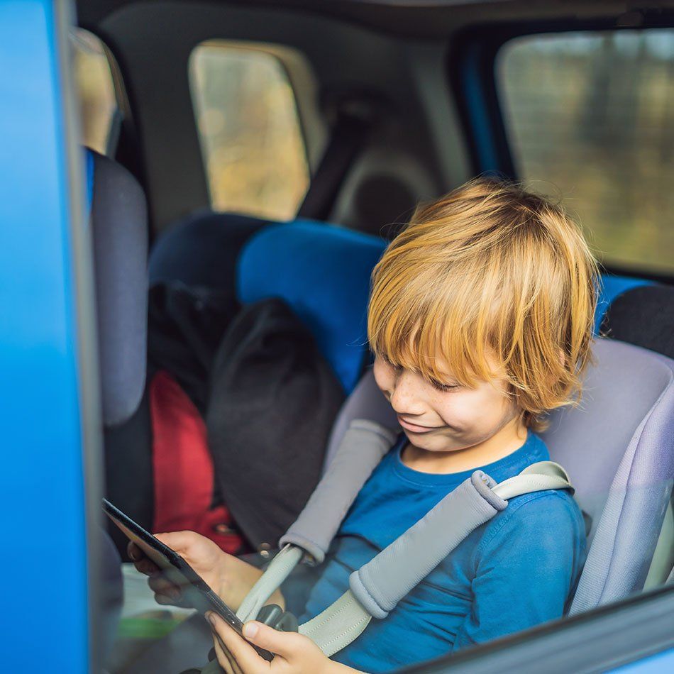 Enfant assis à l'arrière d'un taxi dans un siège pour enfant et qui consulte une tablette numérique