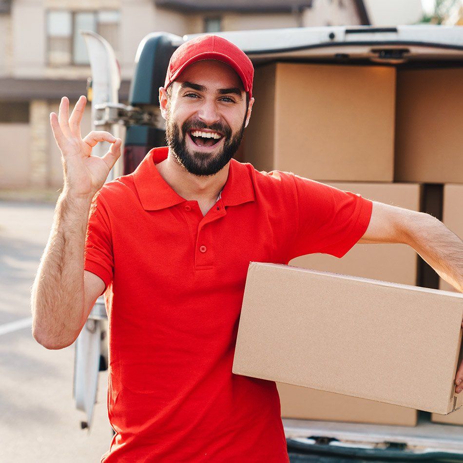 Homme souriant portant un carton de déménagement devant un fourgon de transport