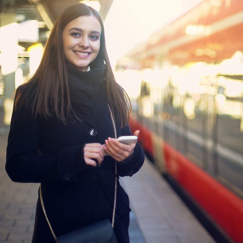 Femme souriante sur un quai de gare avec un téléphone portable dans les mains