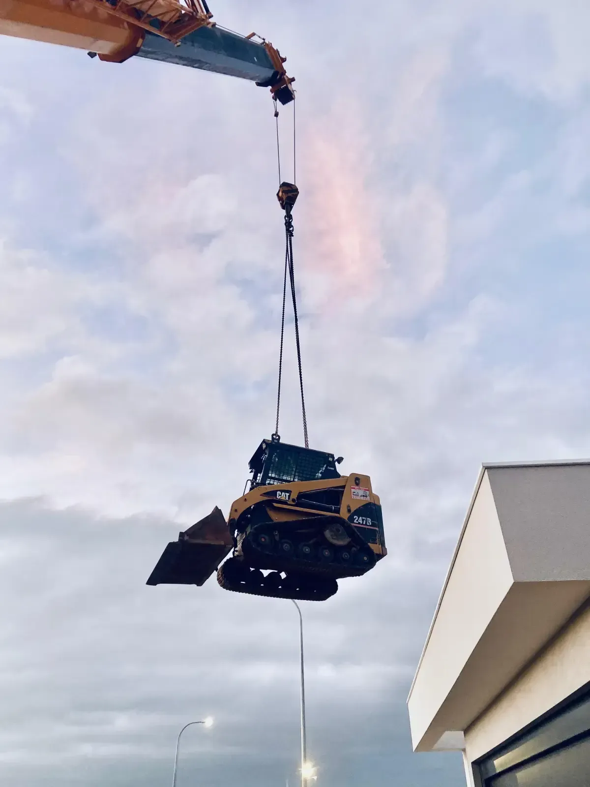 Una pequeña excavadora está suspendida mediante un cable de grúa contra un cielo nublado.