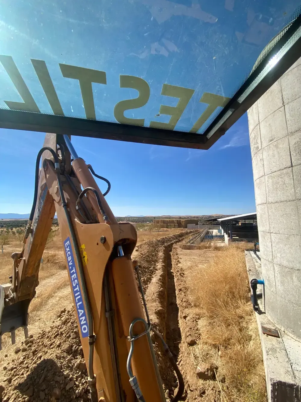 Excavadora cavando una zanja junto a una estructura de hormigón en un día soleado.