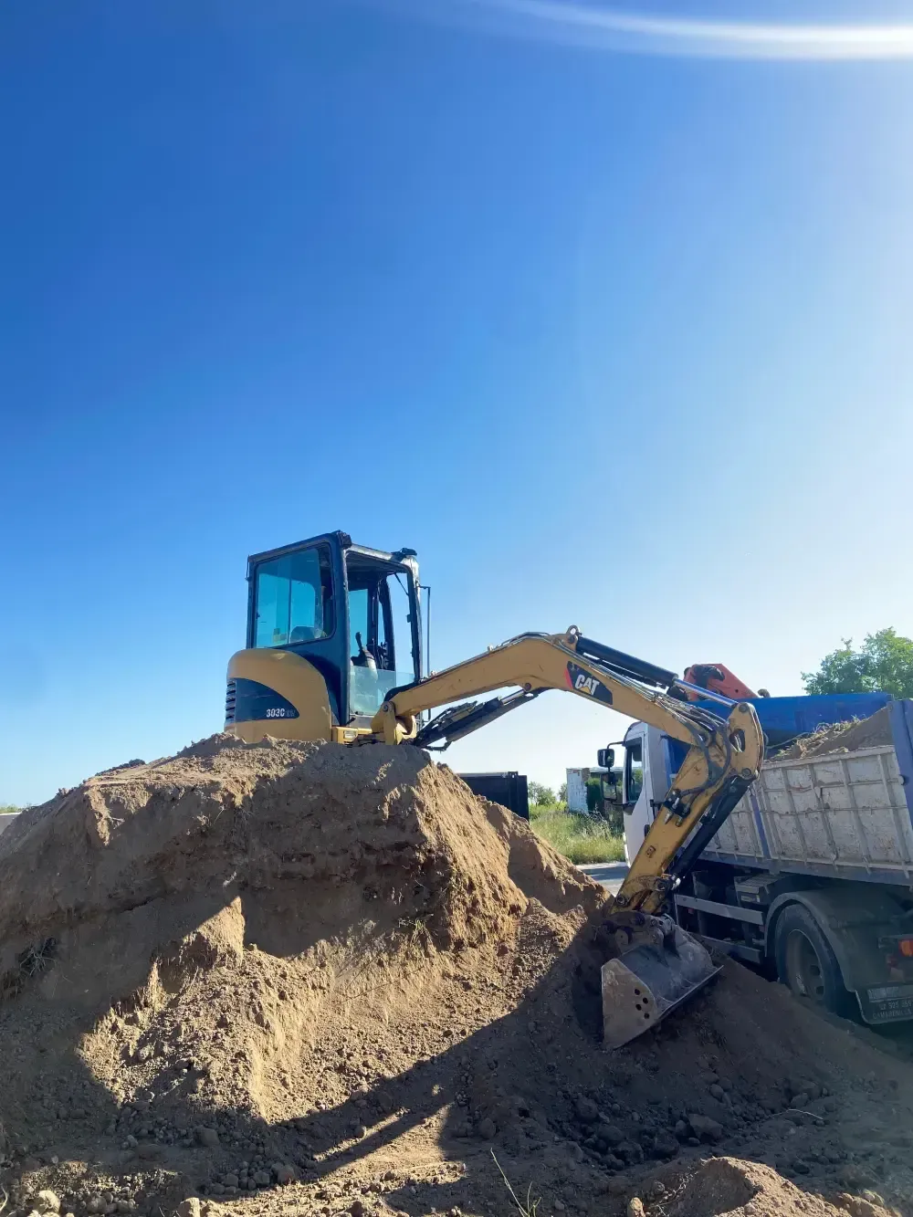 Excavadora cargando tierra en un camión volquete bajo un cielo azul claro.