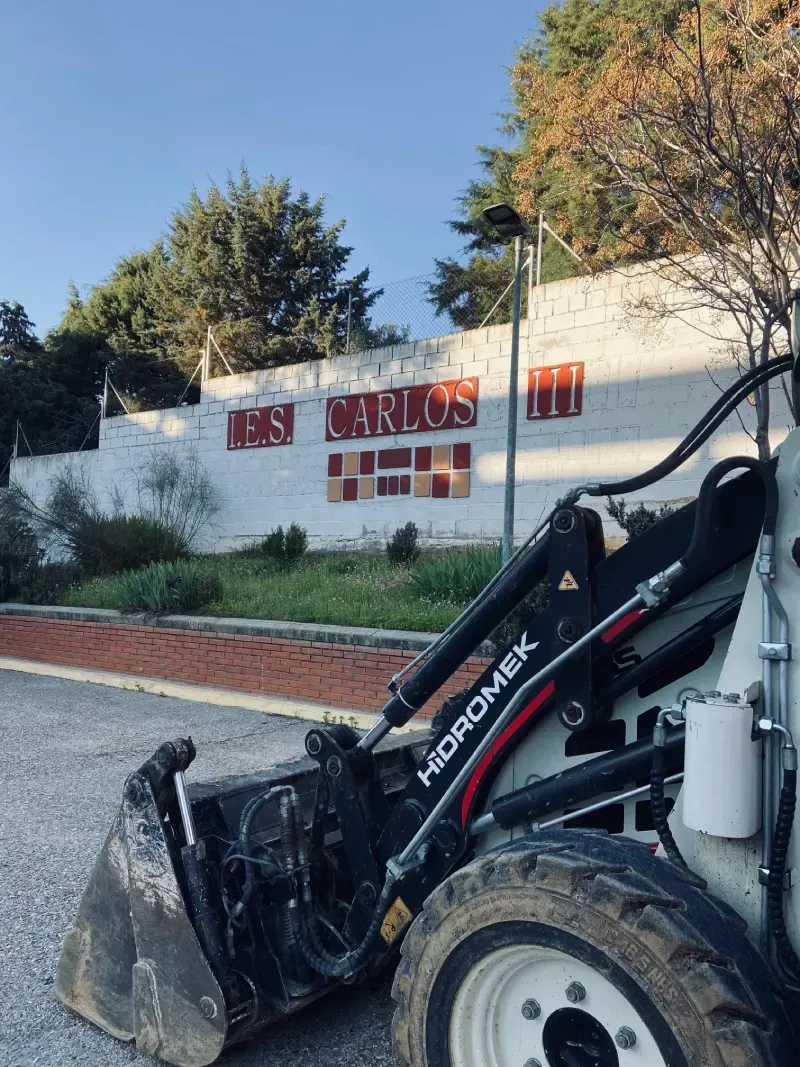 Cargadora de dirección deslizante frente a una pared blanca con letras rojas descoloridas, al aire libre.