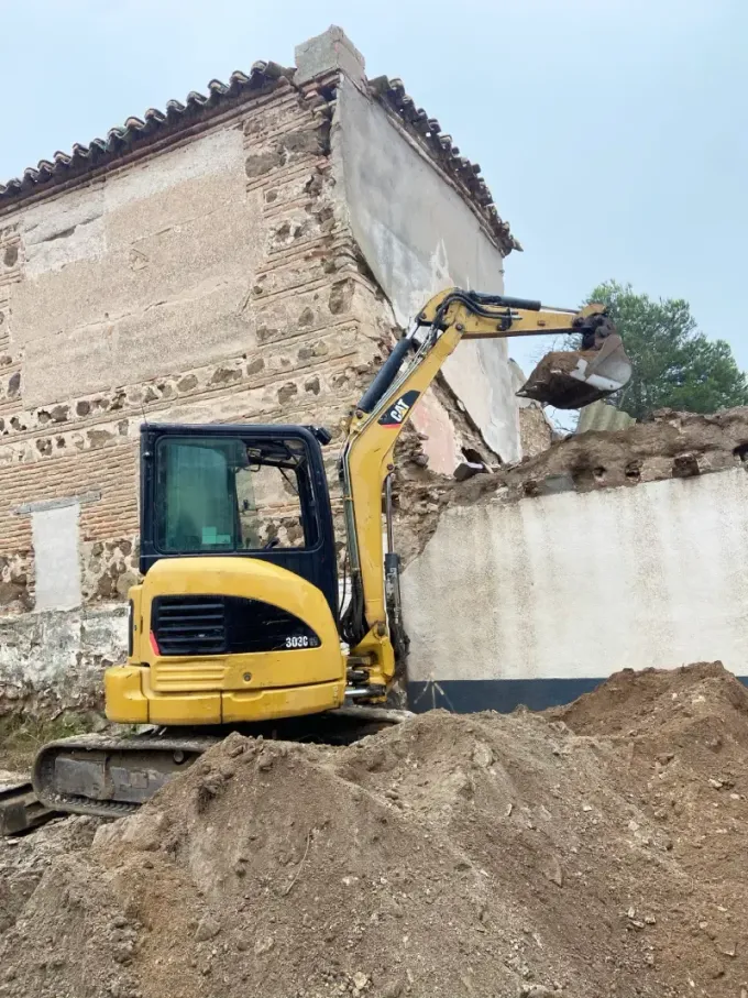 Excavadora amarilla demoliendo un edificio de ladrillos; sitio de construcción.