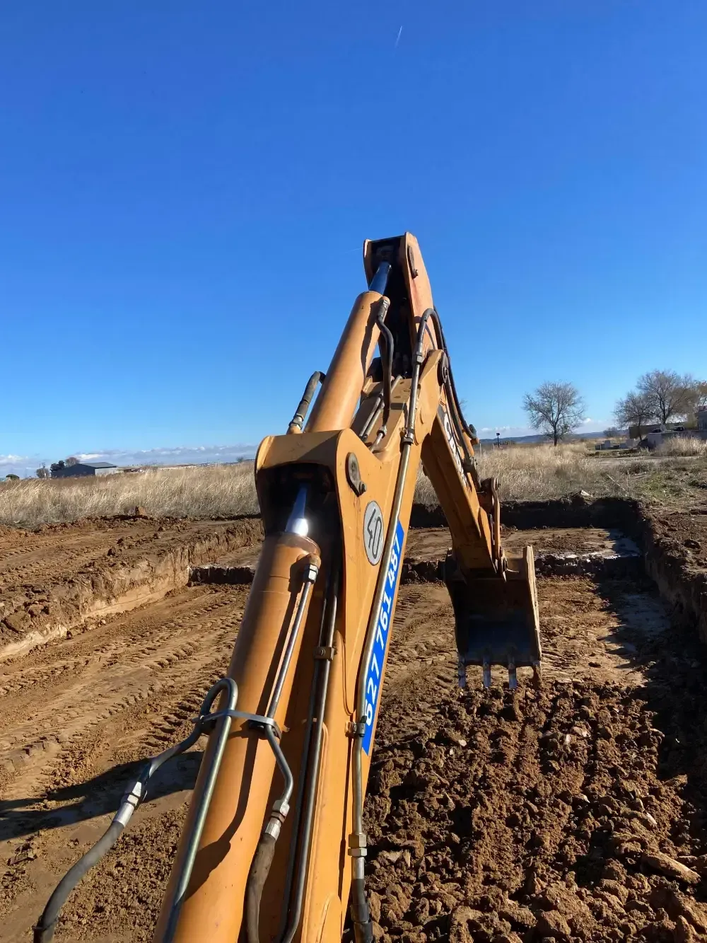 Una excavadora cavando una zanja en suelo marrón, bajo un cielo azul brillante.