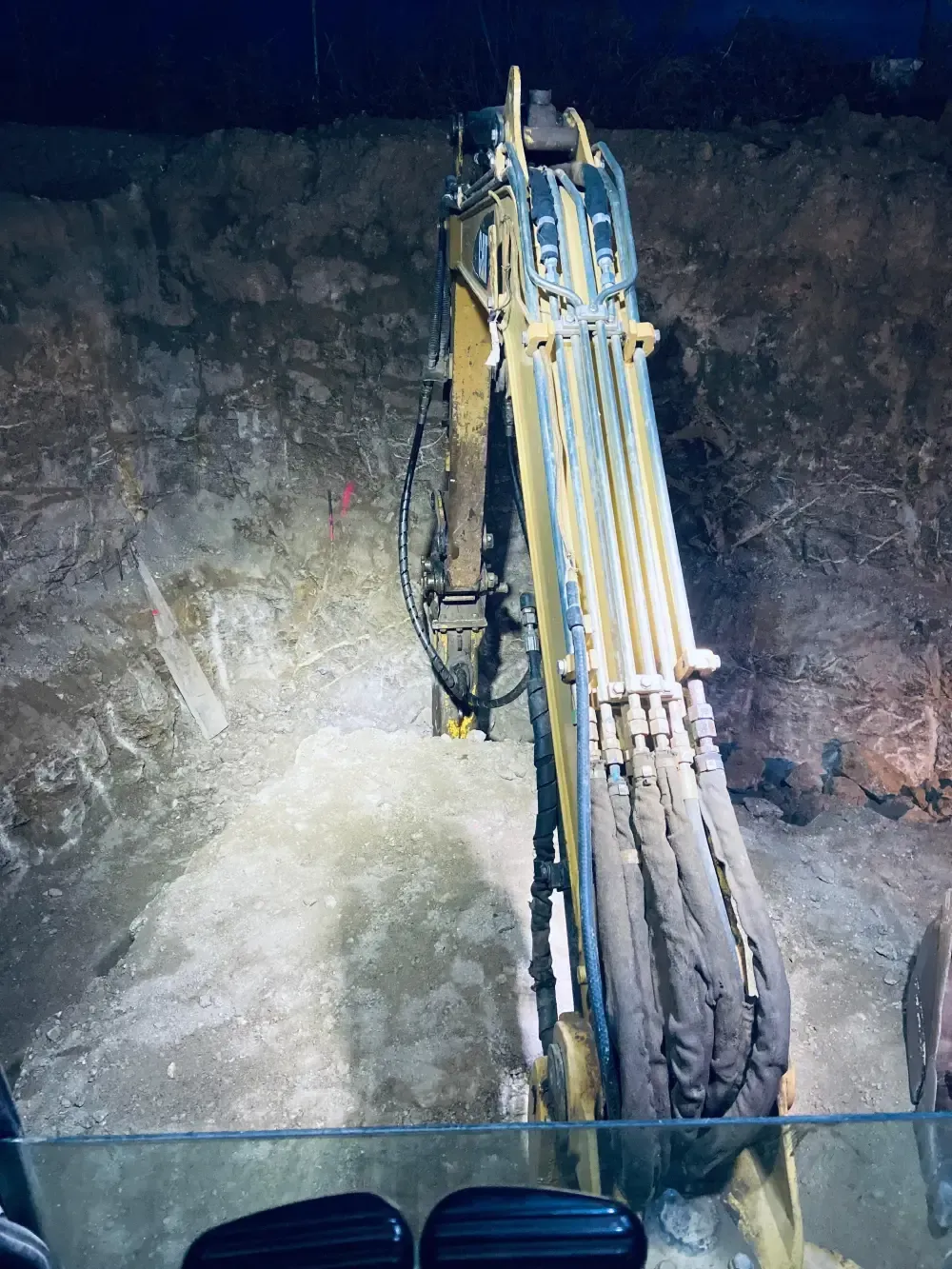 Brazo de excavadora en un túnel, excavando en una pared de roca. Oscuro, con algo de luz iluminando el trabajo.