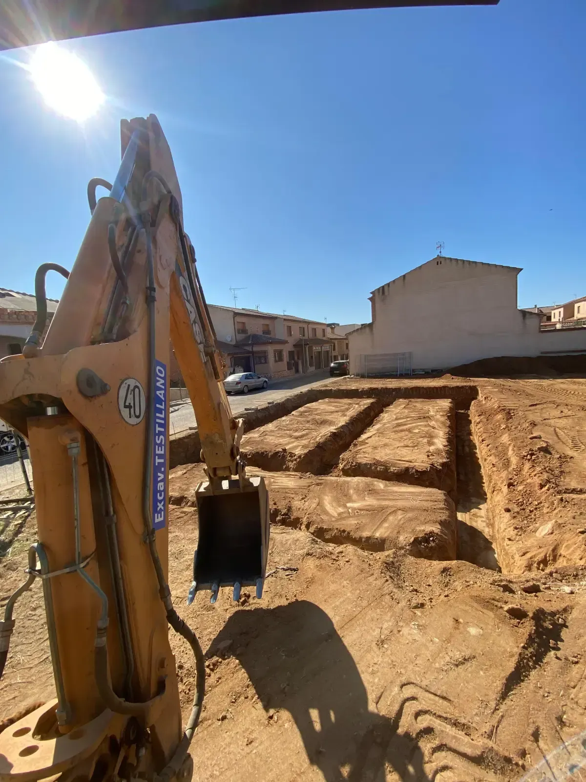 Excavadora en sitio de construcción con zanjas de cimentación, día soleado, fondo residencial.
