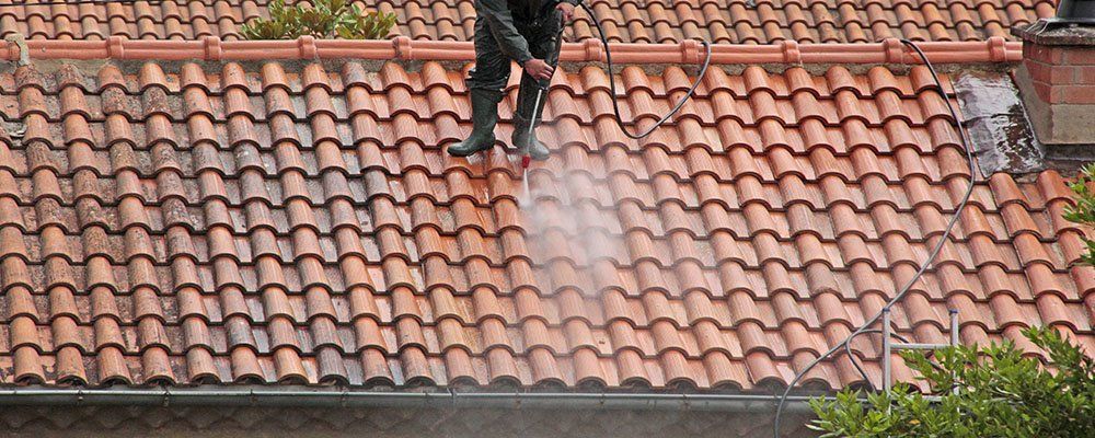 Un homme décape la toiture au nettoyeur à haute pression