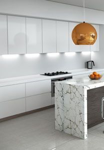 Cuisine moderne blanche avec îlot en marbre, suspension dorée et éclairage sous les meubles.