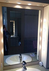 Miroir de salle de bain avec éclairage intégré, reflétant un lavabo, un robinet et une armoire.