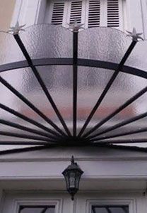 Auvent en métal noir et en verre au-dessus d'une porte blanche avec une lanterne.