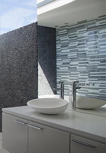 Salle de bains avec mur en pierre, crédence en mosaïque, plan de travail blanc et vasque.