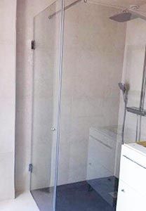 Cabine de douche en verre dans une salle de bains avec pommeau de douche et carrelage gris.