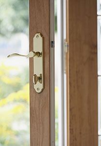 Une porte en bois à poignée en laiton est entrouverte, laissant entrevoir le paysage verdoyant extérieur.