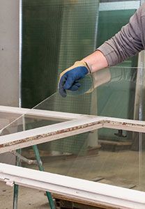 Une personne portant un gant bleu tient une vitre au-dessus du cadre de la fenêtre.
