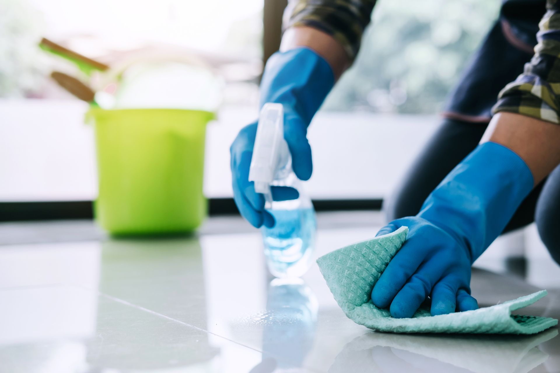Eine Person mit blauen Handschuhen reinigt den Boden mit einem Tuch.