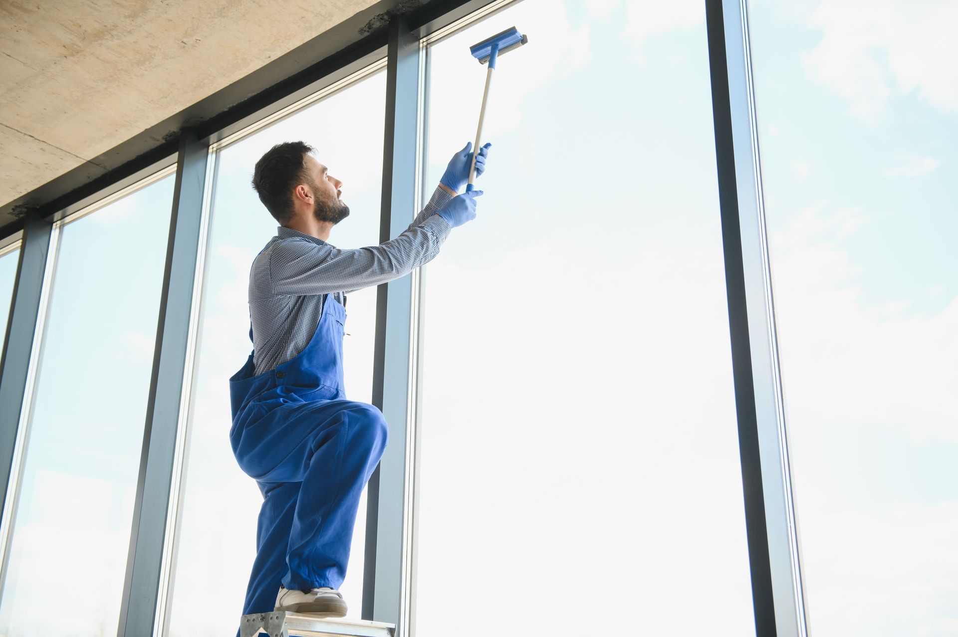 Ein Mann putzt auf einer Leiter stehend ein Fenster mit einem Abzieher.