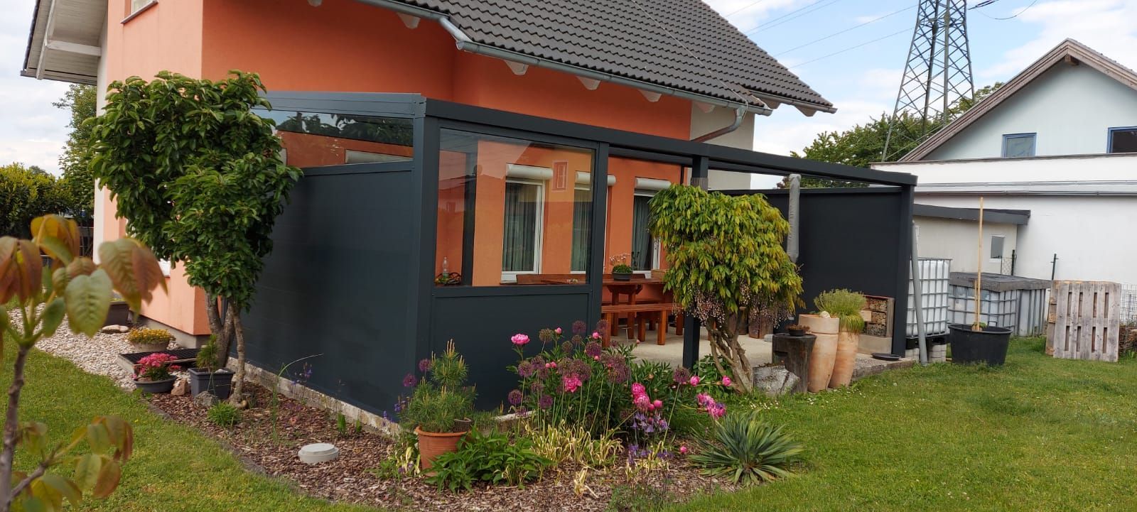 Dunkelblauer Außenschirm auf einer Terrasse, an einem Vordach befestigt, neben einer Wand.